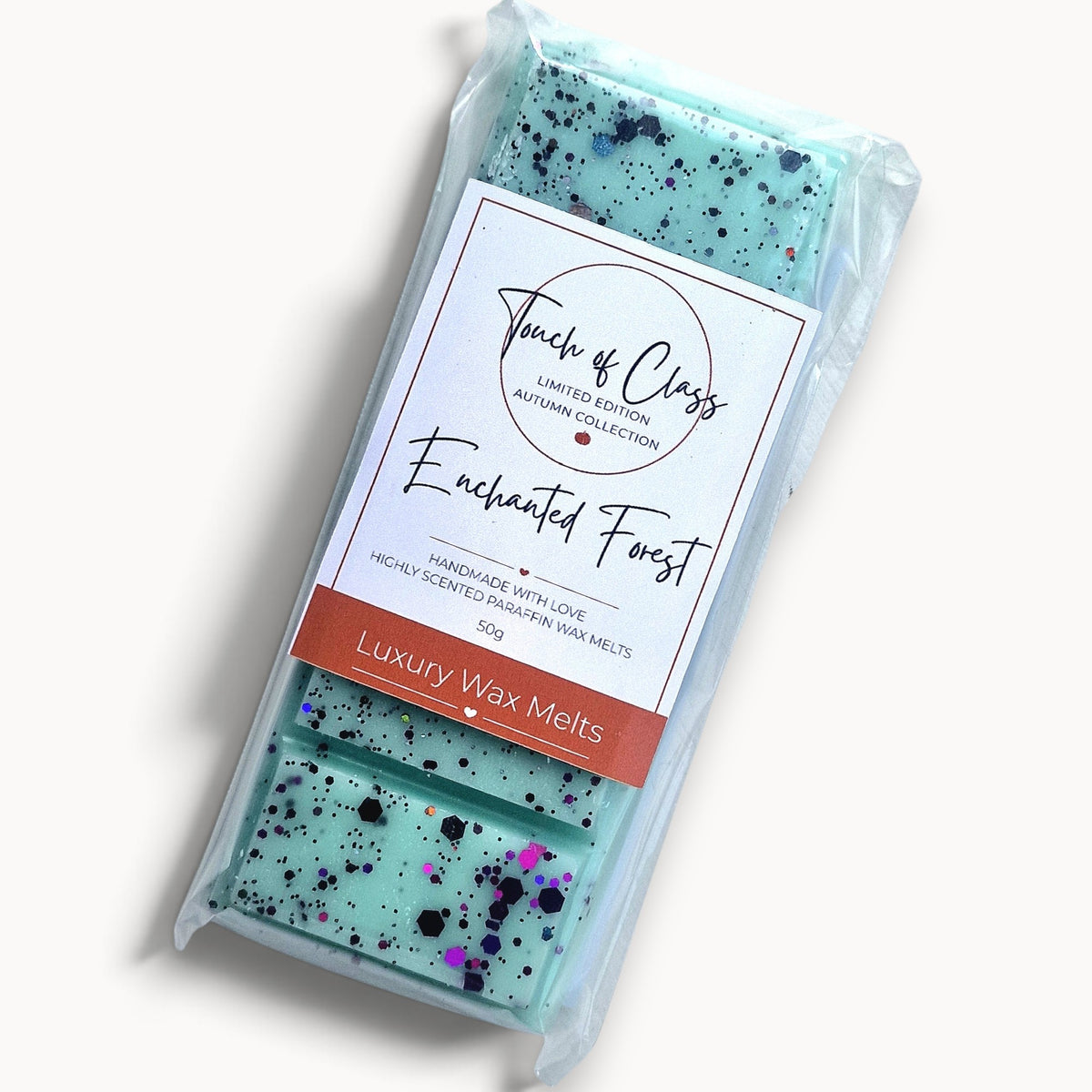 A packaged bar of wax melt from Touch of Class, featuring a mint green base with black and purple glitter flecks, wrapped in clear plastic with a white and orange label.