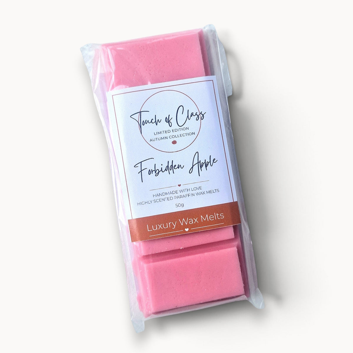 A package of Touch of Class 'Forbidden Apple' luxury wax melts, showing pink wax blocks visible through a clear plastic bag with a white and brown label.